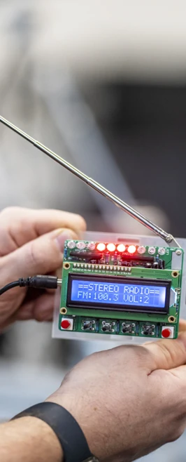 Close-up of a small electronic device with an LCD screen displaying radio frequency settings, held by a person in a technical lab. Close-up of a small electronic device with an LCD screen displaying radio frequency settings, held by a person in a technical lab.